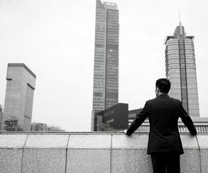 a black and white photo of a person standing and viewing a business building