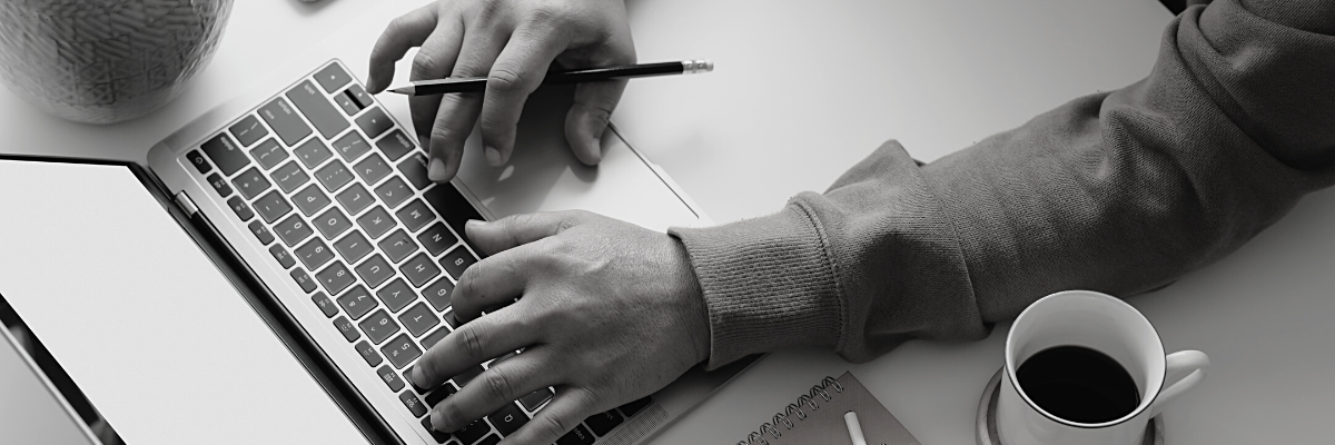 a black and white photo of a person working on a laptop with a cup of coffee