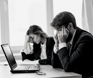 a black and white photo of two people sitting at a desk behind a laptop