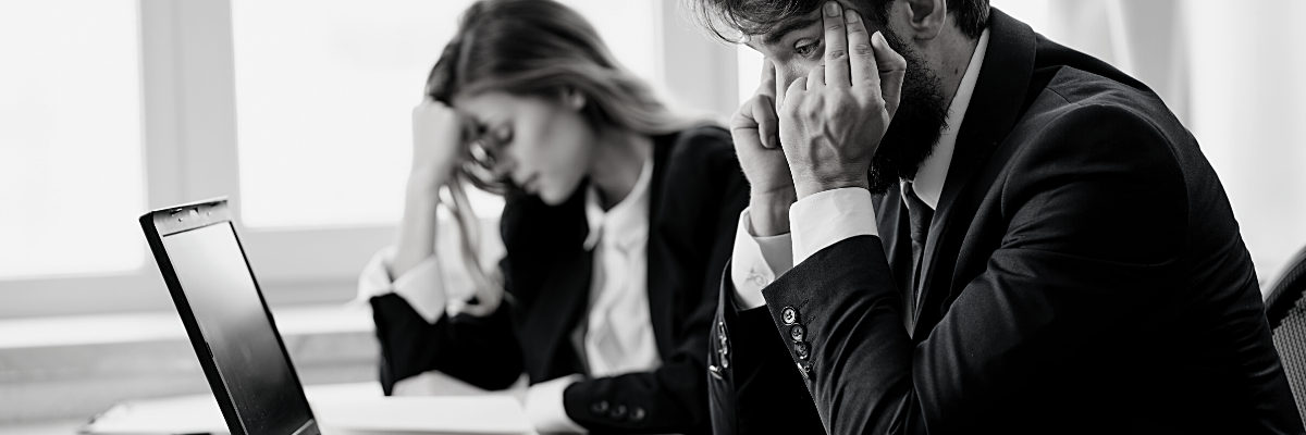 a black and white photo of two people sitting at a desk behind a laptop