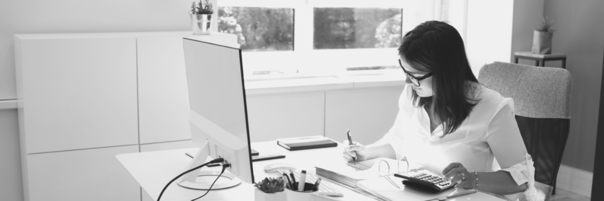 a black and white photo of a lady sitting behind a desk with a computer calculating her financials