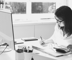 a small black and white photo of a lady sitting behind a desk with a computer calculating her financials