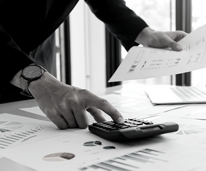 a small black and white photo of some financial reports with a hand using the calculator