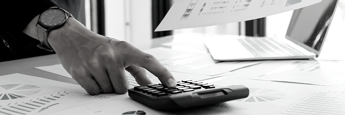 a black and white photo of some financial reports with a hand using the calculator