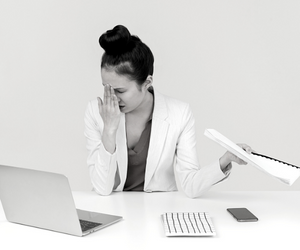a small black and white photo of a very tired woman sitting at a table in front of a laptop