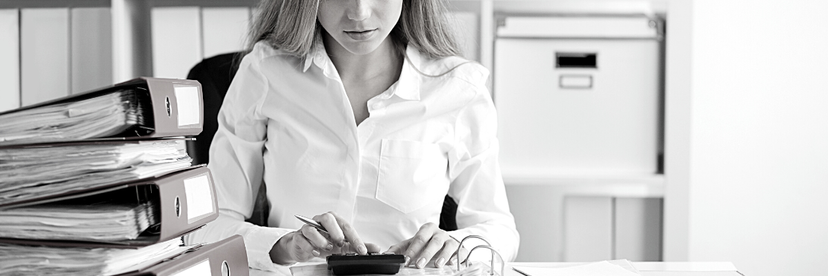 a black and white photo of a lady sitting at a desk with a set of files using her financial calculator