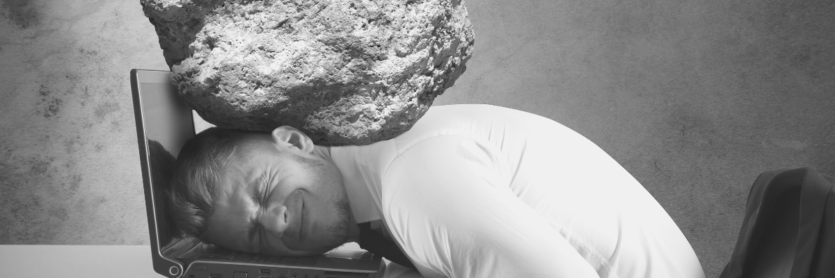 a black and white photo of a male with his head on a laptop feeling the crunch of a rock on his head